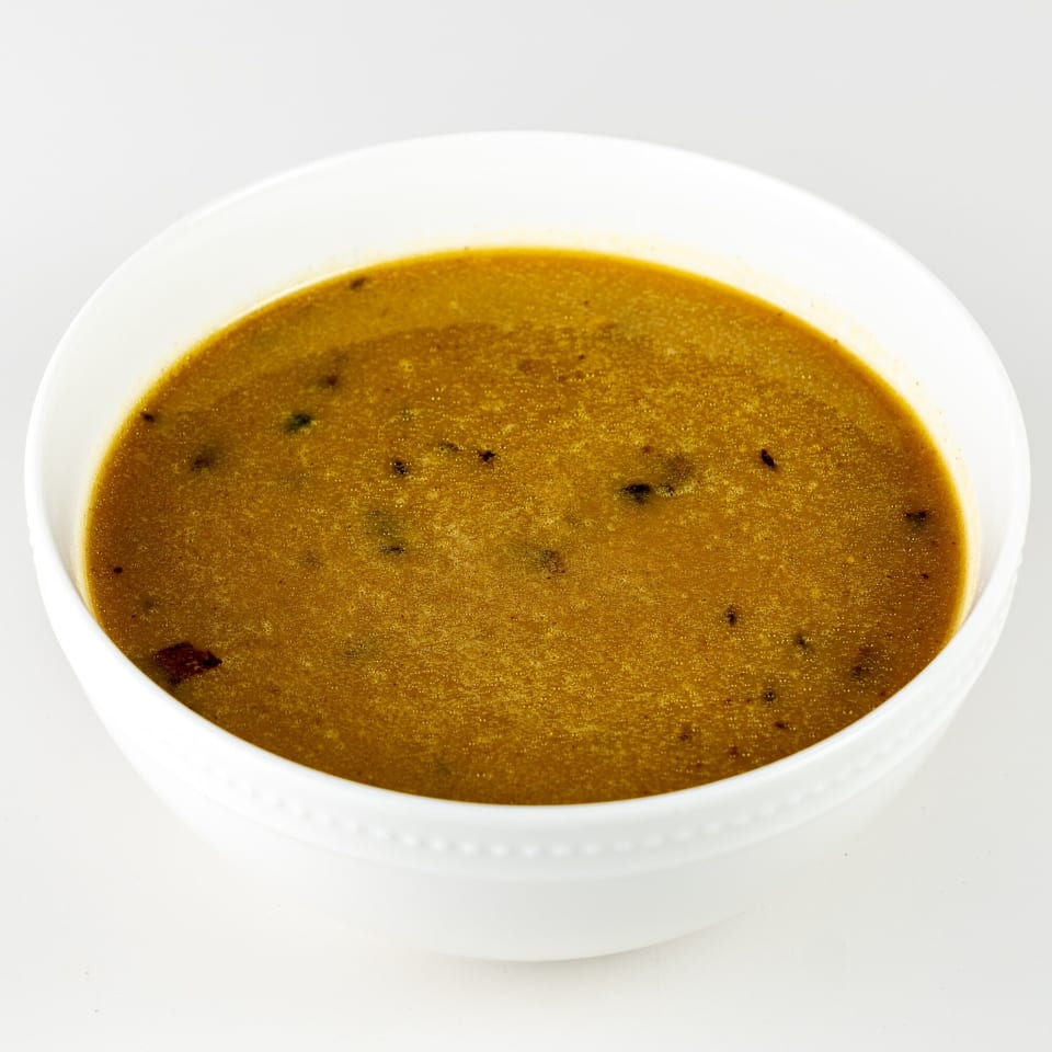A white bowl filled with a rich, golden-brown Caribbean soup, garnished with dark spices.