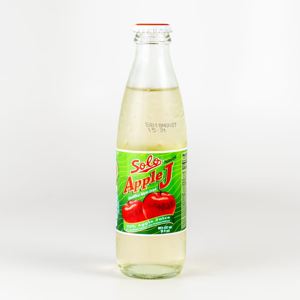 A glass bottle of Solo Apple J sparkling apple drink with a green label and red apples.