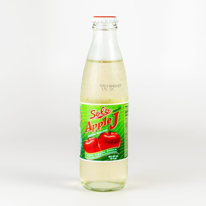 A glass bottle of Solo Apple J sparkling apple drink with a green label and red apples.