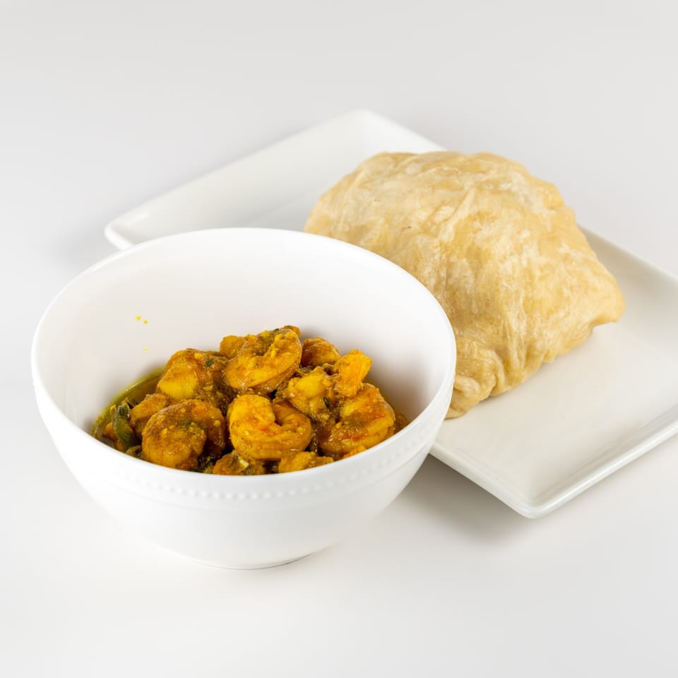 Taste of Trini's curry shrimp in a white bowl, with a flatbread on a white plate.