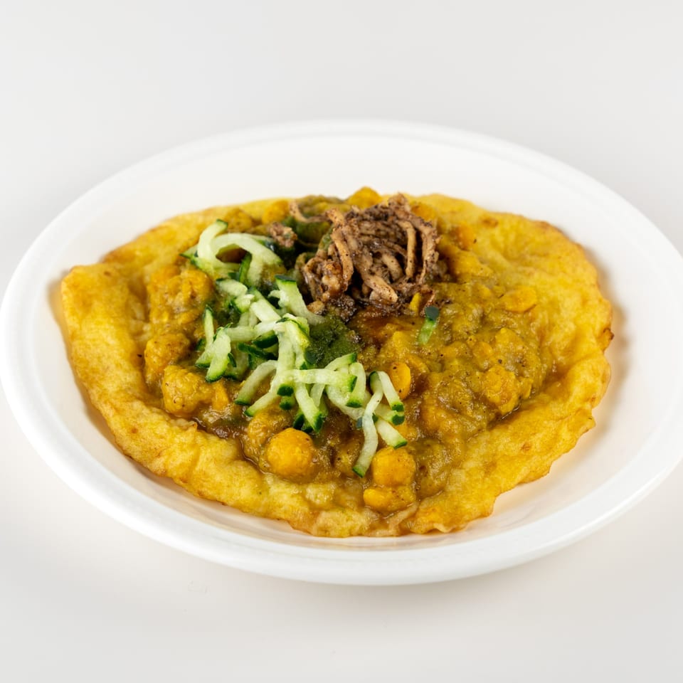 A Taste of Trini doubles dish with curried chickpeas, cucumber, and shredded meat on a white plate.