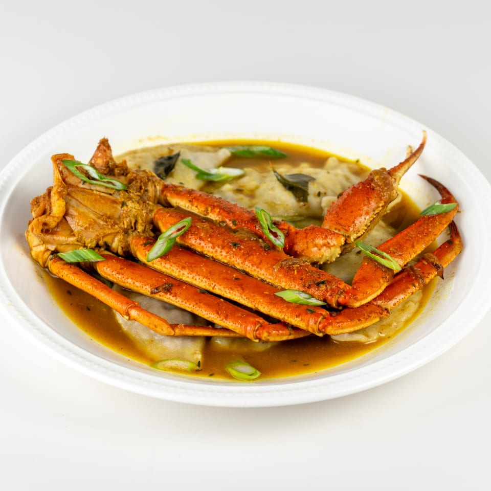 Taste of Trini's crab and dumplings in a rich, savory broth, garnished with green onions.