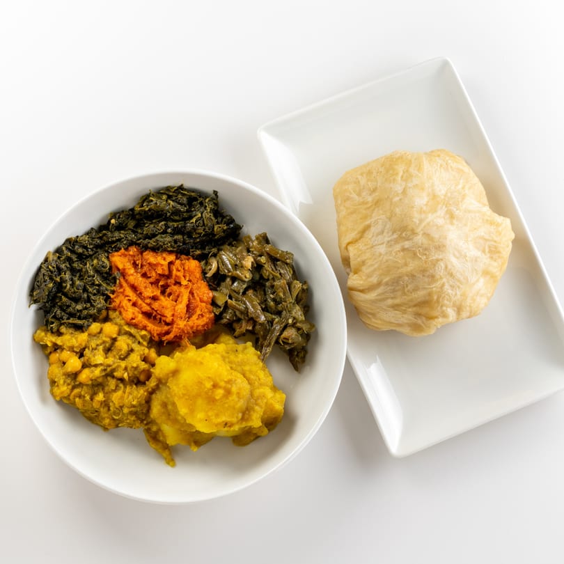 A bowl of Caribbean food with various colorful dishes and a flatbread on a white plate.