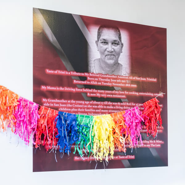 A tribute poster for Ameeran Ali, with her black and white portrait and text, adorned with colorful streamers.