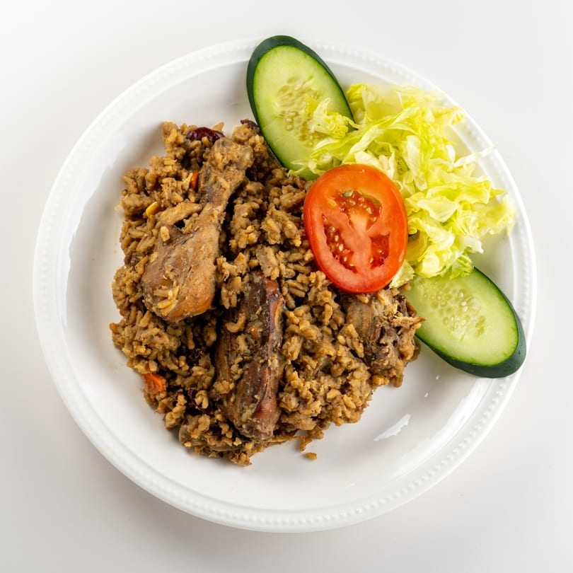 Taste of Trini's Caribbean pelau with chicken, rice, and a side salad with cucumber and tomato.